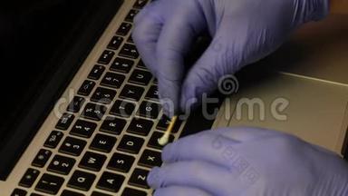 一个戴橡胶手套的人正在清洗他的笔记本电脑。 棉签清洁钥匙。 然后他用一个特殊的键盘擦拭笔记本电脑键盘